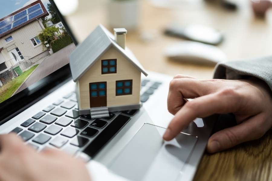 Une petite maquette de maison posée sur le clavier d'un ordinateur portable pendant une recherche en ligne.