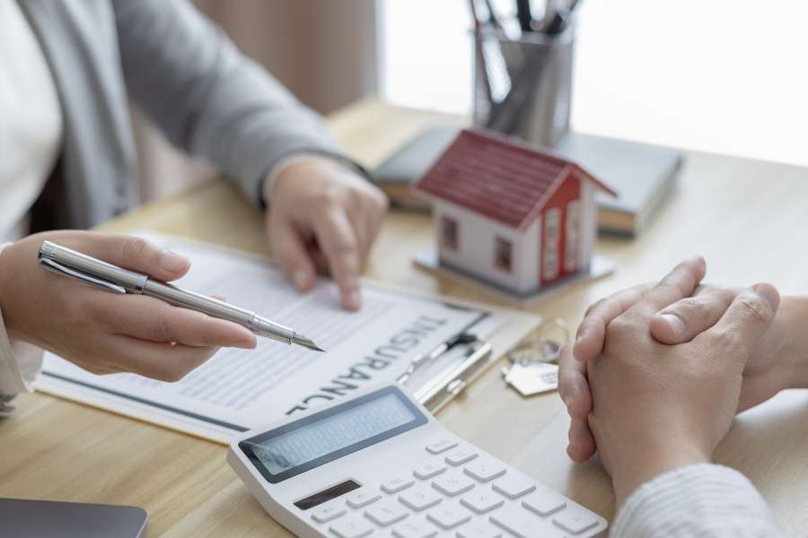 Une personne pointe un document du doigt avec un stylo à côté d'une calculatrice et d'une maquette de maison, illustrant l'évaluation du prix d'un bien immobilier.