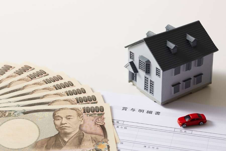 Des billets de banque, une maquette de maison et une petite voiture rouge posées sur des documents financiers, illustrant un simulateur de prêt immobilier.