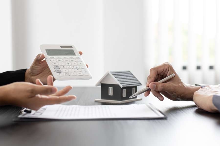 Des personnes discutent d'un devis d'assurance habitation avec une maquette de maison et une calculatrice.