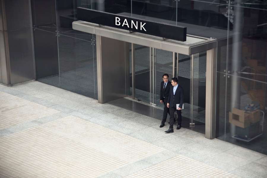Deux hommes en costume sortent de l'entrée vitrée d'un grand bâtiment moderne portant l'enseigne "Bank".